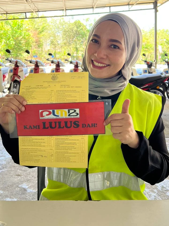 Pelajar PLMB yang baru lulus ujian JPJ, memegang borang ujian dan papan 'Kami Lulus Dah!'